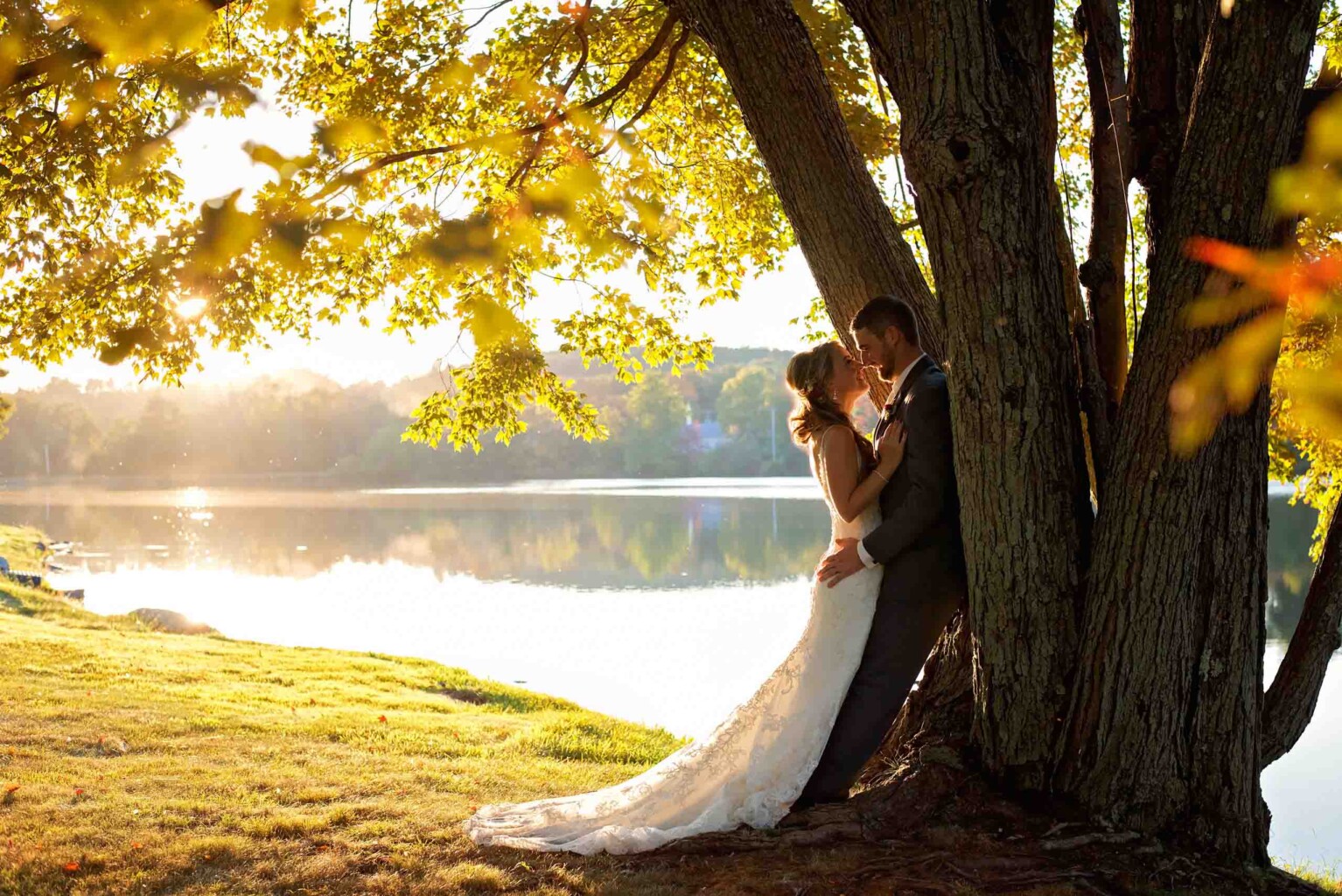 Couple kissing against lakeside tree.