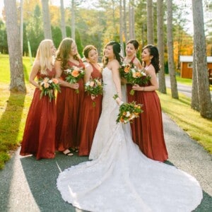 bridal party in red dresses under trees.