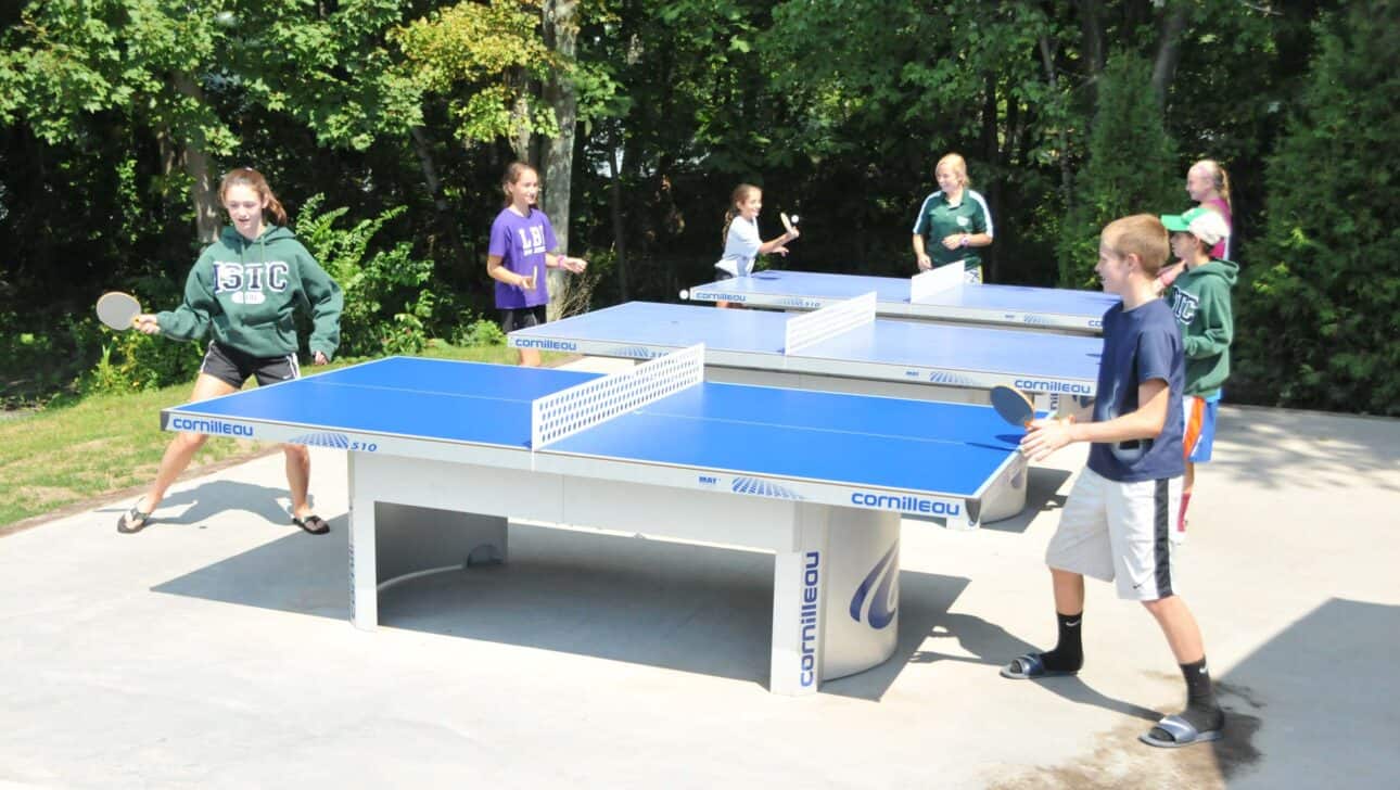 table tennis being played by kids outside.