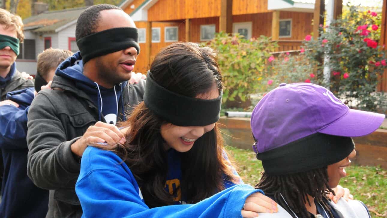blindfolded teens in team building activity outside.