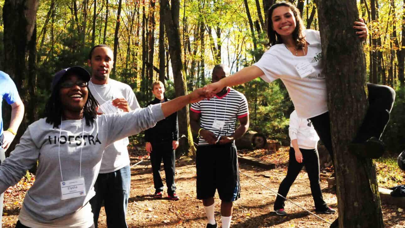 teens holding hands on tightrope in woods.