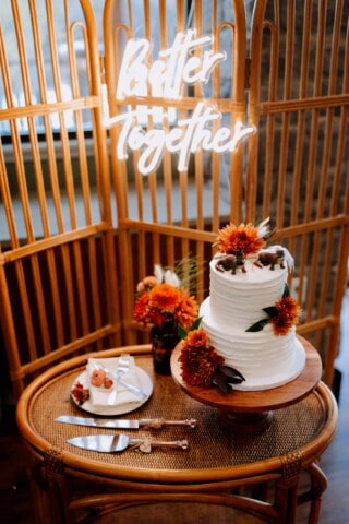 wedding cake in front of a neon sign that says better together.