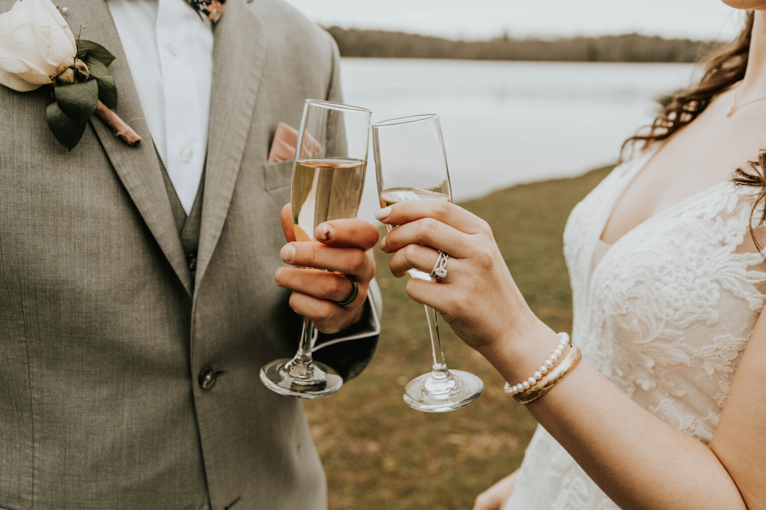 close-up-of-couples-holding-their-champagne-glasses-infront-of-lake.