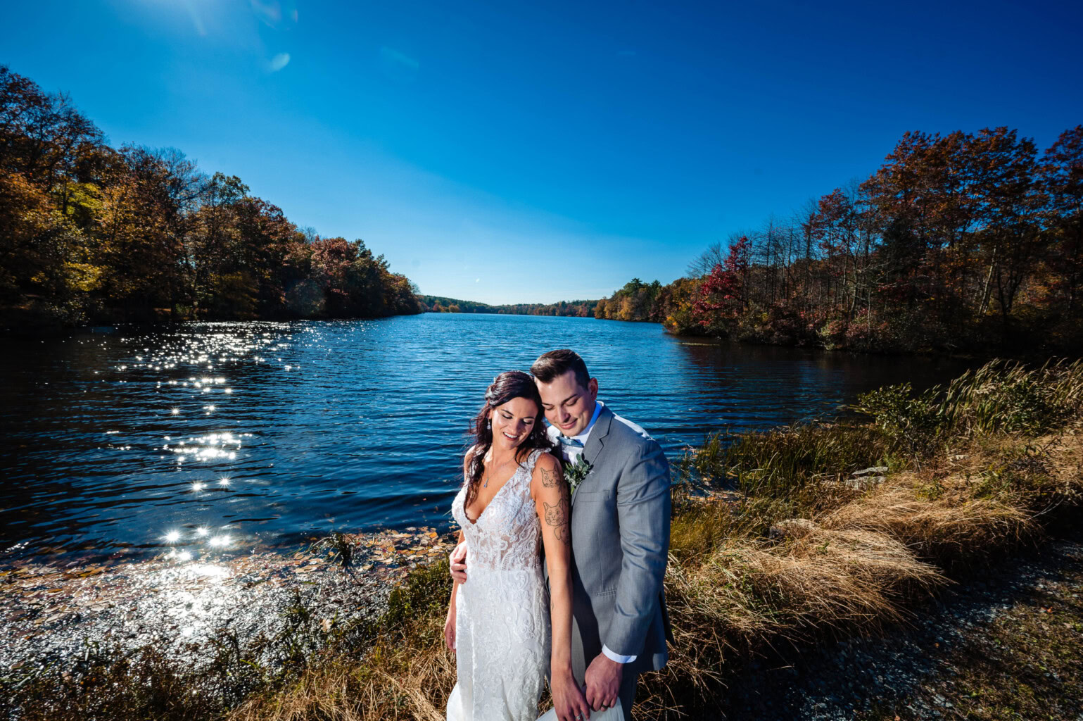 Couple posed at the end of the lake with a bright blue sky.