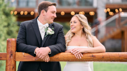 Couple smiling and talking while leaning against the wooden fence.